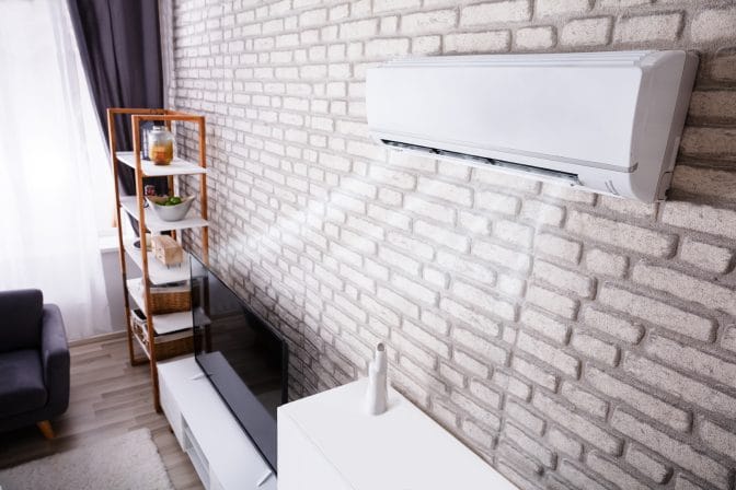 White Air Conditioner Blowing Cold Air On Brick Wall In Living R